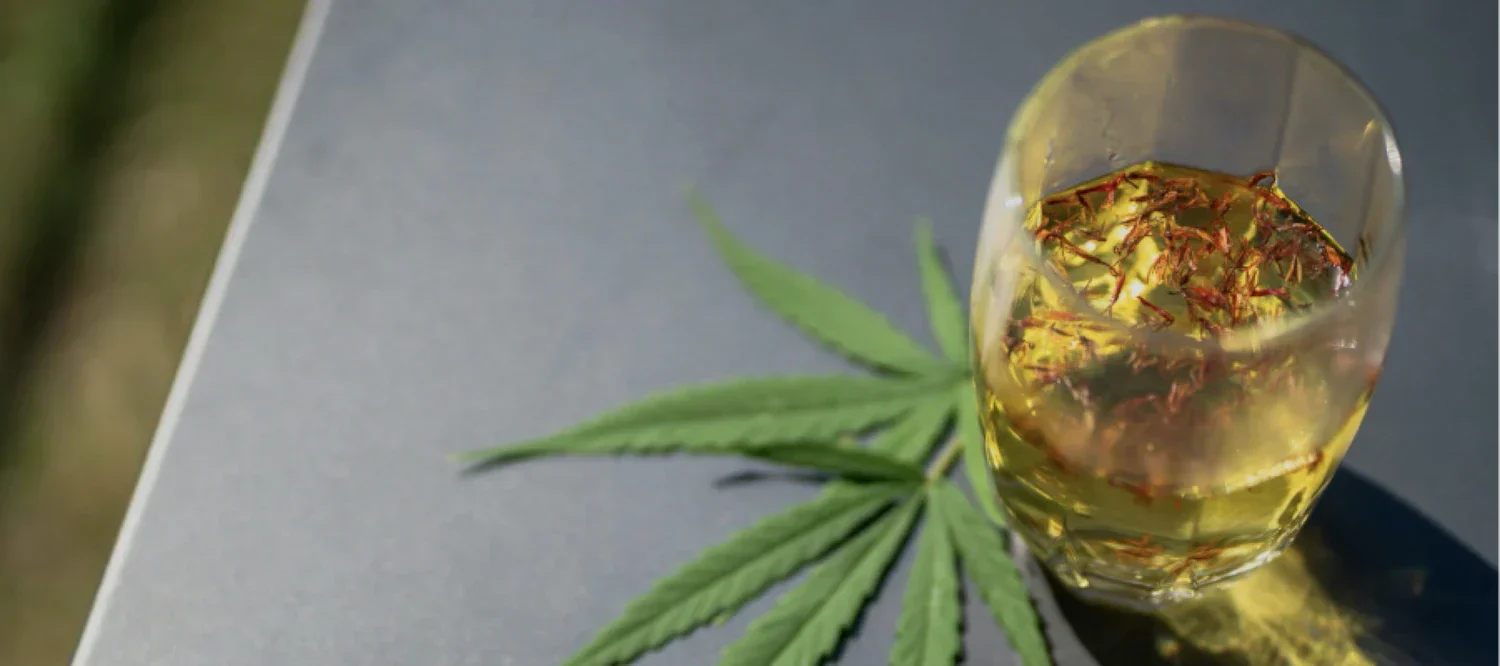 Cannabisblatt neben einem Glas mit Alkohol